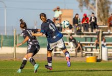 Duas jogadoras disputam a bola durante uma partida de futebol feminino ao ar livre.