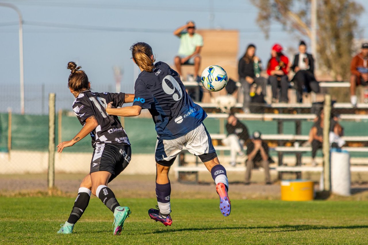 Duas jogadoras disputam a bola durante uma partida de futebol feminino ao ar livre.