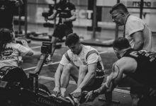 Atletas competem em uma sessão de remo em ergômetros dentro de uma academia.