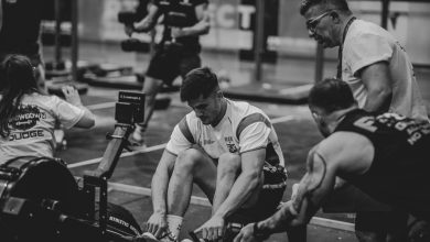 Atletas competem em uma sessão de remo em ergômetros dentro de uma academia.