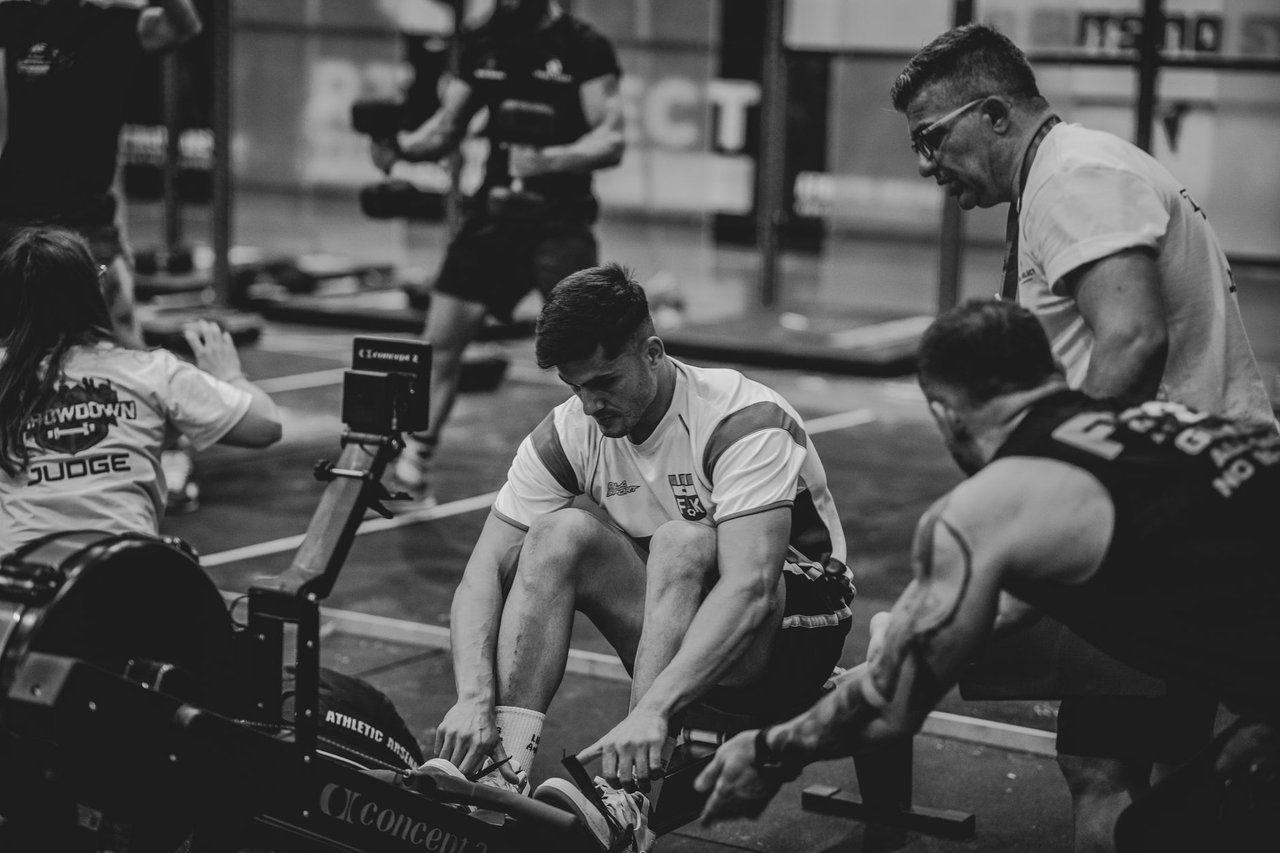 Atletas competem em uma sessão de remo em ergômetros dentro de uma academia.