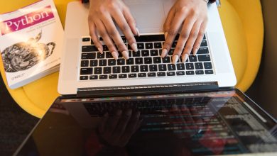 Pessoa digitando em um laptop durante uma sessão de programação, com um livro sobre Python ao lado.
