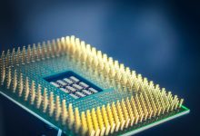 Close de um chip de processamento com pinos dourados sobre fundo azul.