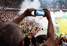 Torcedores registram com smartphones uma partida de futebol nas arquibancadas de um estádio.