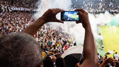 Torcedores registram com smartphones uma partida de futebol nas arquibancadas de um estádio.
