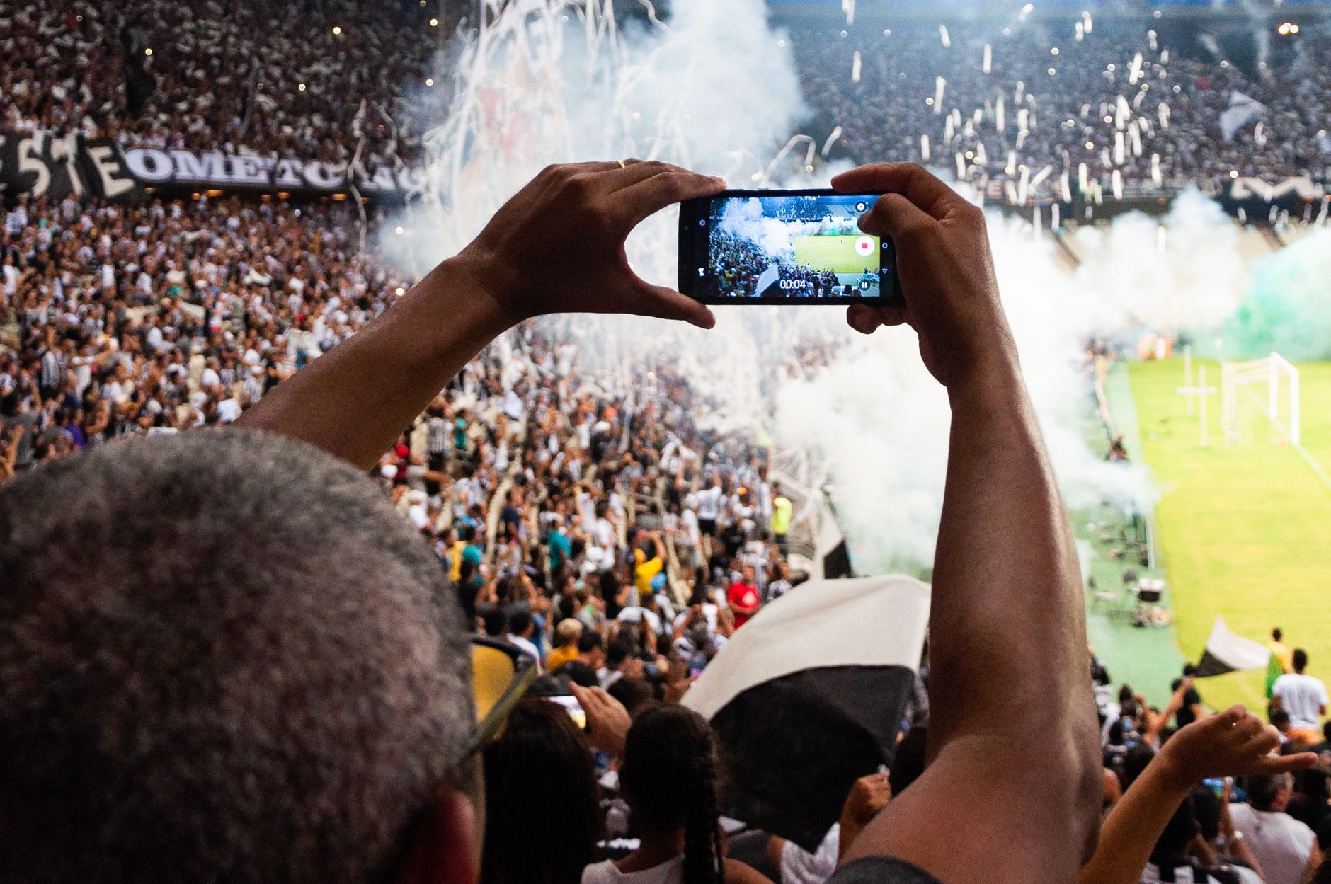 Torcedores registram com smartphones uma partida de futebol nas arquibancadas de um estádio.
